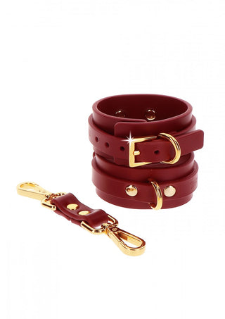 TabooM Handbojor - Bondage har röda lädermanschetter med guldspännen och ett avtagbart spänne, perfekt för att lägga till elegans till din bondage-samling. Utställda mot en vit bakgrund visar de upp livfulla färger och hantverk.