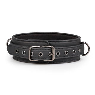 Bdsm Halsband Med Koppel är ett svart syntetläderbälte med ett silverspänne, öljetter och dubbla sidoringar mot en vit bakgrund.