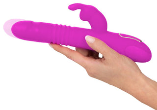 En hand håller en Thrusting Pearl Rabbit Vibrator i rosa, gjord av kroppssäkert silikon, med kaninörondesign för förbättrad g-punktstimulering.
