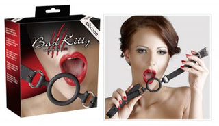 En kvinna poserar med Gag - Bad Kitty - Silikon O-Gag och håller munnen öppen. Förpackningen visar sitt namn och framhäver dess lockelse som ett unikt BDSM-redskap.
