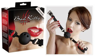 En elegant låda märkt "Gag - Bad Kitty - Small Silicone Gag" visar en silikon gag boll, hållen av en kvinna med livfulla rött läppstift och naglar, vilket tyder på anpassningsbar komfort med dess justerbara rem.