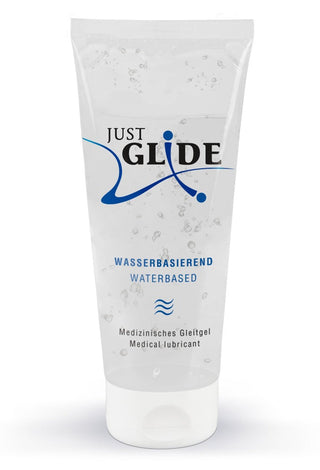 Just Glide Waterbased Glidmedel" är förpackad i en klar tub med blå och svart text på tyska och engelska. Designen är enkel, med vågliknande mönster och en vit keps.