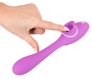 En hand vaggar försiktigt 2 Funktion Vibrator Med Tunga - 22 cm, en lila silikonmassager med en sugkoppsände för mångsidig njutning, vilket säkerställer en oförglömlig G-punkt-upplevelse varje gång.