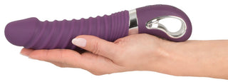 En hand håller en lila räfflad Vibrerande dildo med värmefunktion med ett silverringhandtag, tillverkad av flytande silikon och med 12 vibrationslägen för olika sensationer.
