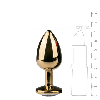 Ett droppformat guldmetalliskt föremål, Guld Metall Buttplug - Med Kristall, sitter elegant bredvid en storleksjämförelsegrafik som liknar läppstift.