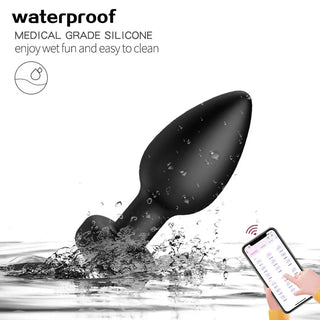 Appstyrd buttplug-vibrator i svart silikon med elegant design, visad i vatten tillsammans med en hand som håller i en smartphone-kontroll.