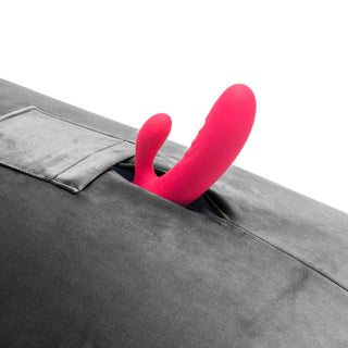 Ett rosa, böjt föremål dyker upp ur en ficka i en grå tygyta, som påminner om den innovativa designen hos Humphrey Liberator Sexkudde.