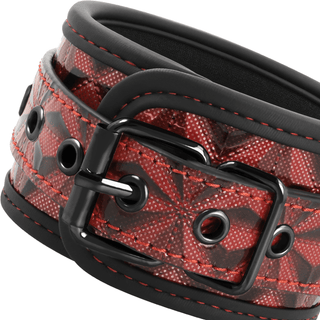 En närbild av BegMe Red Premium Handbojor visar ett svart och rött veganskt läderbälte med ett geometriskt mönster, med ett svart metallspänne och öljetter. Den röda kalejdoskopdesignen erbjuder en elegant, modern atmosfär som är lämplig för dem som utforskar bondage-lekar.
