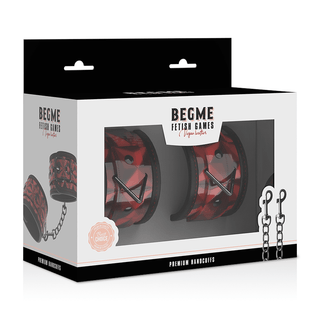 Förpackningen för "BegMe Red Premium Handbojor" innehåller ett par röda och svarta vadderade manschetter gjorda av veganskt läder med metallkedjor, tillsammans med en logotyp och illustrationer, idealiska för bondage-lekar-entusiaster.
