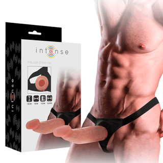 En muskulös person visar den Intense Hollow Harness Strap-on, gjord av ftalatfritt TPR-material, medan han står bredvid dess förpackning.