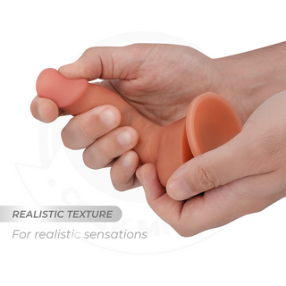 En hand som klämmer på Cock Miller Böjbar Dildo 15cm, en köttfärgad, realistisk texturerad dildo tillverkad av silikon av medicinsk kvalitet med en sugbas.