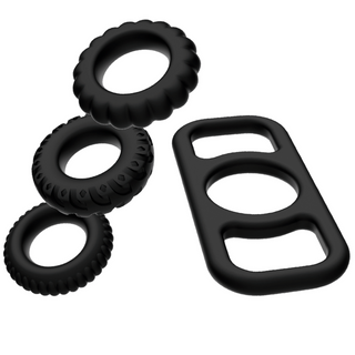 Addicted Toys Cockring Set 4-pack, med fyra svarta silikoncockrings och ett rektangulärt svart gummitillbehör med rundade kanter, visas på en vit bakgrund.