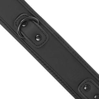 Närbild av en BDSM-tillbehör som heter "Fetish Neoprene Halsband & Koppel", med en svart läderrem prydd med två metall D-ringar och svarta nitar. Den har slät struktur, sydda kanter och symmetriska detaljer för en elegant touch.