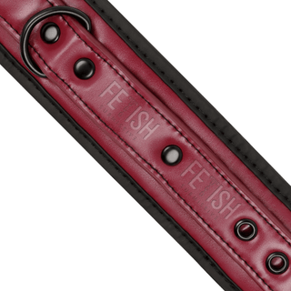 En närbild av ett rött och svart veganskt läderband med metallringar, präglade upprepade gånger med "FETISH" - perfekt för BDSM-nybörjare. Produkt: Handbojor med neoprenfoder.