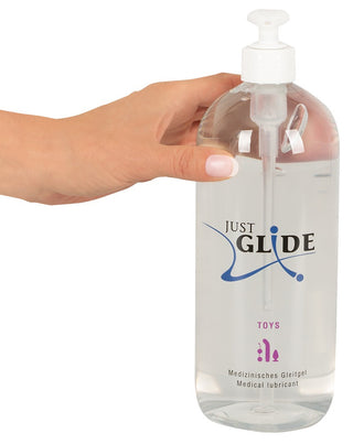 En hand håller en stor flaska Just Glide Toys Glidmedel med pumpdispenser, perfekt för att öka komforten med latexkondomer eller utforska nya sensationer med sexleksaker.