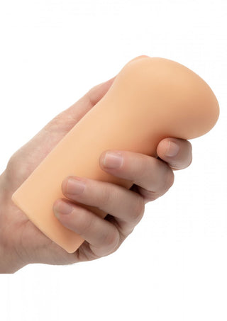 En hand håller Lösvagina The Flight Attendant, ett beige cylindriskt föremål tillverkat av Pure Skin-material, med en slät struktur mot en vanlig vit bakgrund.