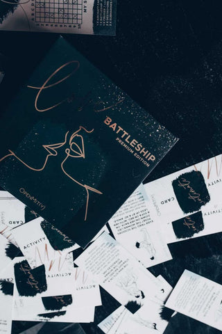 Love Battleship Premium Edition erbjuder spännande gameplay med en elegant, mörk låda med en linjekonstdesign. Abstrakta aktivitetskort utspridda på den mörka bakgrunden lovar en spännande strategisk utmaning.