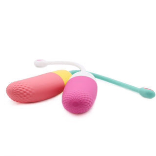 Två rosa personliga massageapparater i silikon, liknande Magic Motion Vini - Vibrerande Ägg, har texturerade spetsar och gröna sladdar, vilket ger en appstyrt sexleksak-upplevelse.