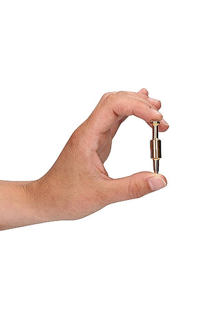 En hand visar elegant upp en liten mässingsfärgad "Magnetiska Nipple Clamps"-adapter mot en orörd vit bakgrund, som utstrålar en lyxkänsla av elegans och precision.