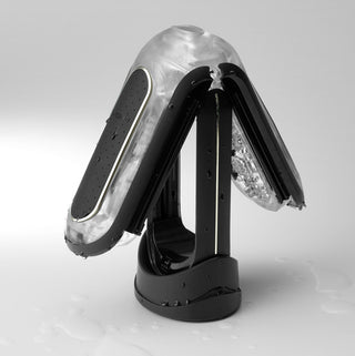 Tenga Fliphole Zero: En elegant, kantig pryl i futuristiskt silver och svart med vattendroppar på ytan. Den har tre vikbara paneler och står på en rund svart bas mot en ljusgrå bakgrund.