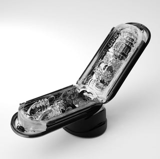 Tenga Fliphole Zero är en svart, genomskinlig elektronisk enhet med invecklade interna växlar och texturer. Den har ett gångjärn som gör att den kan öppnas som en flip-telefon och är inställd mot en vanlig vit bakgrund.