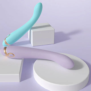 Två pastellfärgade G-Punkt-vibratorer i silikon med böjda former, placerade på minimalistiska plattformar mot en ljuslila bakgrund.