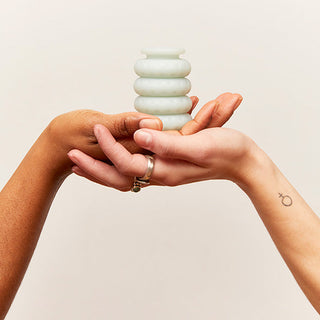 Två händer håller försiktigt en liten, spiralformad vas mot en neutral bakgrund, vilket frammanar den eleganta designen hos OHNUT - Classic Soft Buffer Rings.