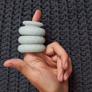Balancing OHNUT - Klassiska mjuka buffertringar i vit stenfärg på ett finger mot en strukturerad grå tygbakgrund.