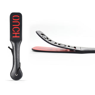 Paddel Piska Med Text är en svart läderpaddel med "OUCH" i rött. Den har ett handtag och handledsögla, med bilder som visar hela paddeln och dess flexibilitet när den ligger platt.