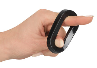 En hand håller försiktigt en svart, oval penisring från Rebel MBS Ball Stretching Kit mot en orörd vit bakgrund.