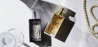 PheroStrong By Night Men 50ml flaska, svart med gulddetaljer, placerad på marmor med ett pärlhalsband bredvid.