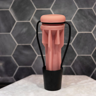 Ett rosa silikonföremål sitter i en svart hållare på en marmoryta med sexkantiga plattor bakom, som liknar Fleshlight Torkställning till form och funktion.