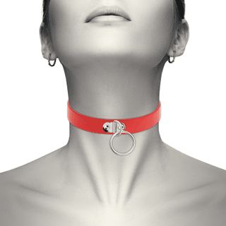 En person bär "Röd Chocker Med Ring", en röd choker med ringdetalj, gjord av veganskt PU läder, mot en gråskalebakgrund.