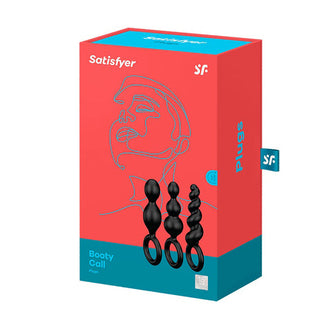 Röd och blå låda med Satisfyer Booty Calls Buttplug 3:a set, med en abstrakt ansiktskonstdesign, tillverkad av flexibel silikon.
