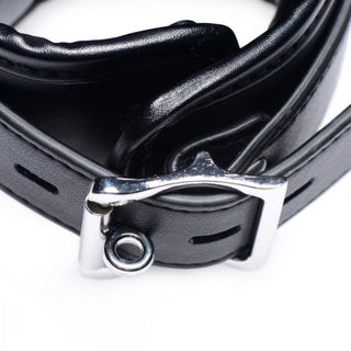 En närbild av Sexkudde - Handbojor & Lår har ett svart läderbälte med ett glänsande silverspänne, som utstrålar en BDSM-stil, mot en vit bakgrund.