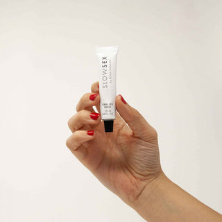 En hand med röda naglar håller en Bijoux Indiscrets - Slowsex Oralsex 10 ml tub, som framhäver dess oralsexförbättrande formel mot en neutral bakgrund.