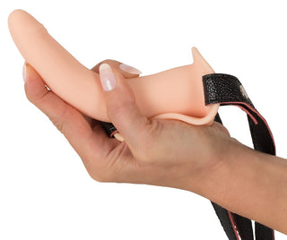 Någon håller Vibrerande Strap-On - Till Henne, med ett beige silikontillbehör med en svart sele, mot en vit bakgrund, vilket framhäver dess eleganta design för en förbättrad upplevelse.