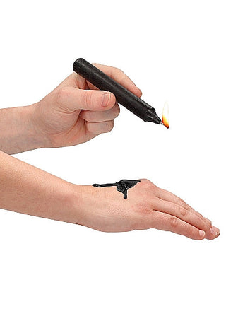 En hand håller ömtåligt en tänd Svart - BDSM Ljus - Vax, med dess vax som sensuellt droppar på baksidan av en annan hand och kastar ett fängslande sken.