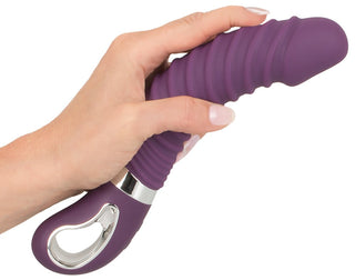 En hand håller Vibrerande dildo med värmefunktion, en lila räfflad silikon leksak för vuxna med en silverhandtagsögla och erbjuder 12 vibrationslägen för en förbättrad upplevelse.