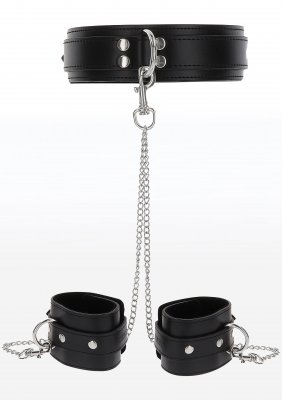 Halsband & Handbojor TabooM, i svart konstläder, har justerbar krage och manschetter sammankopplade med silverkedjor, som fångar essensen av ett diskret bondage-kit mot en vit bakgrund.