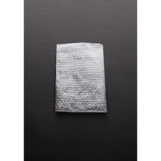 En rektangulär bit bubbelplast ligger på en mörkgrå yta, som påminner om de invecklade mönstren som finns i Ball Crusher-enheter.