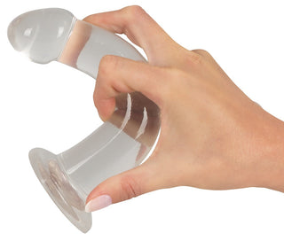En hand håller en genomskinlig, böjd plastbit med en rund bas och topp, som påminner om Realistisk Dildo - Analsex Training Set.