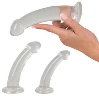 En hand håller den genomskinliga, böjda Realistisk Dildo från Analsex Training Set med en sugbas. Två liknande objekt finns nedan.