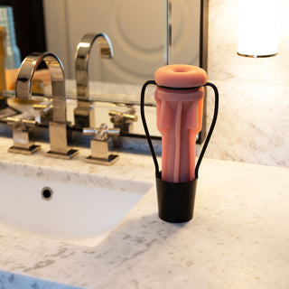 En Fleshlight Torkställning toalettartiklar i silikon torkar i en kopp vid en elegant kran, diskret placerad på den eleganta marmorhandfatet.