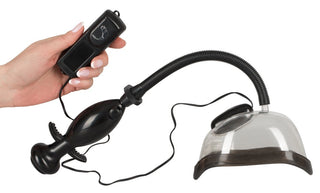 En hand håller en elegant svart fjärrkontroll ansluten till "Vagina Pump Med Vibration - 14 cm", med en plastsuganordning med ett flexibelt rör, vilket förbättrar upplevelsen av att använda denna innovativa sexleksak.