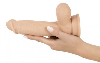 En hand håller Realistixxx Torero Dildo, en hudtonad silikondildo med sugbas och realistisk vibrator, på en vanlig vit bakgrund.