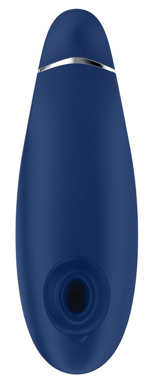 En elegant Womanizer Premium 2, mörkblå och oval, har Pleasure Air™-teknik. Den har en metallring nära toppen och en cirkulär öppning längst ner mot en vit bakgrund.